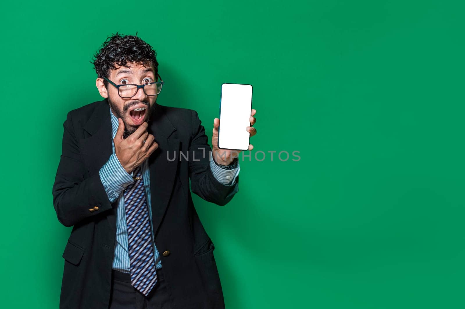 Surprised young businessman showing cell phone screen isolated. Businessman showing an advertisement on the screen of his cell phone. Amazed handsome business man showing cell phone screen.