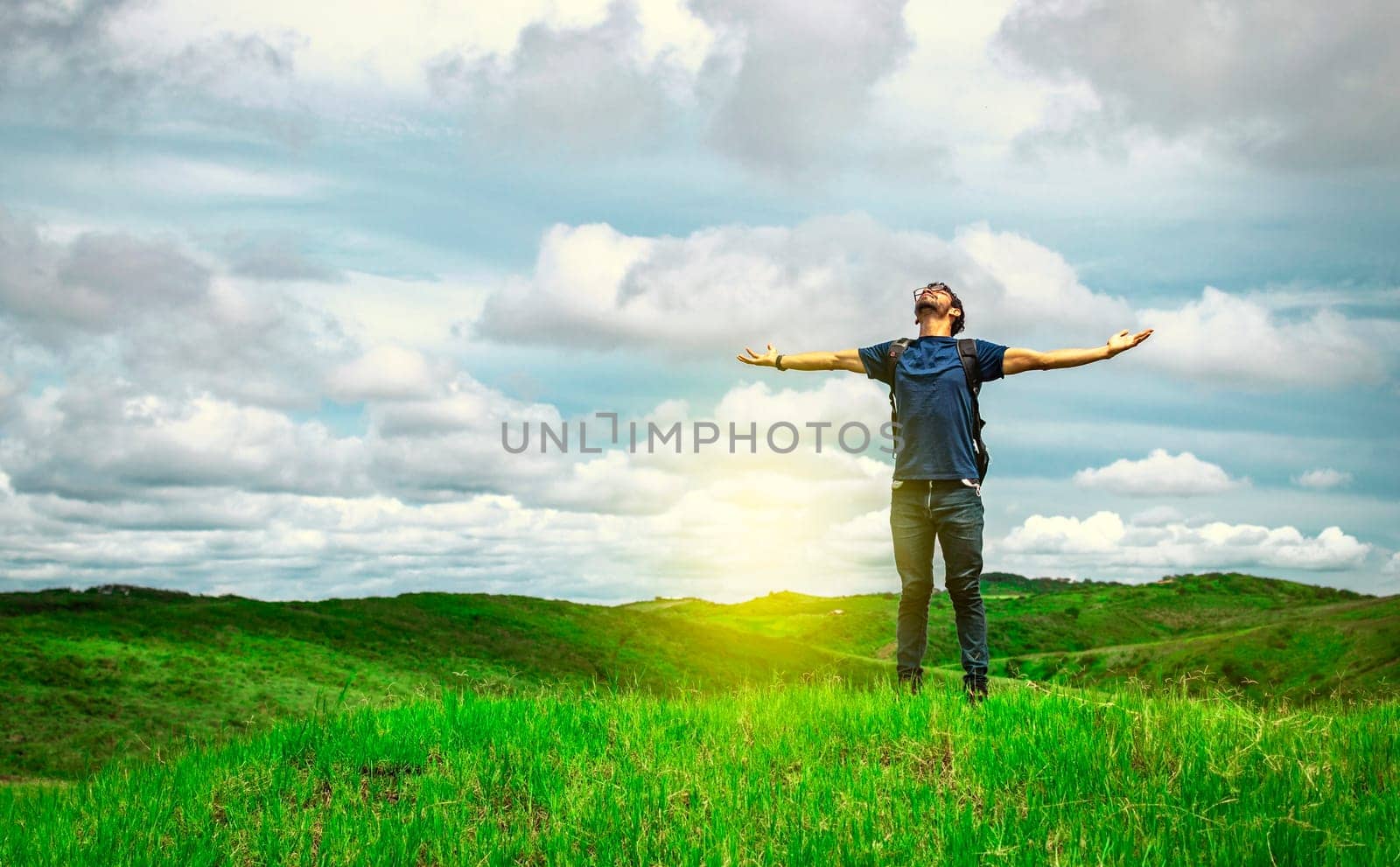 Adventurous man spreading his arms in the countryside. Man with backpack on a hill spreading his arms. Explorer man spreading his arms on a hill. Lifestyle of adventurous man in the field