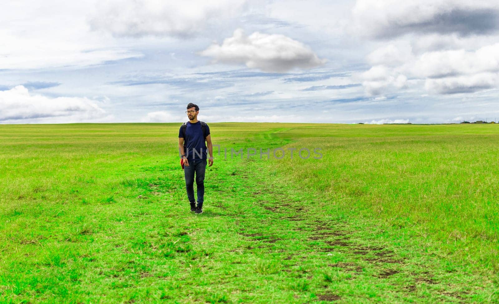 Traveler man walking in the beautiful countryside. Backpacker man walking in a countryside. Landscape of traveler man walking in the green field. Lifestyle of adventurous man in the field