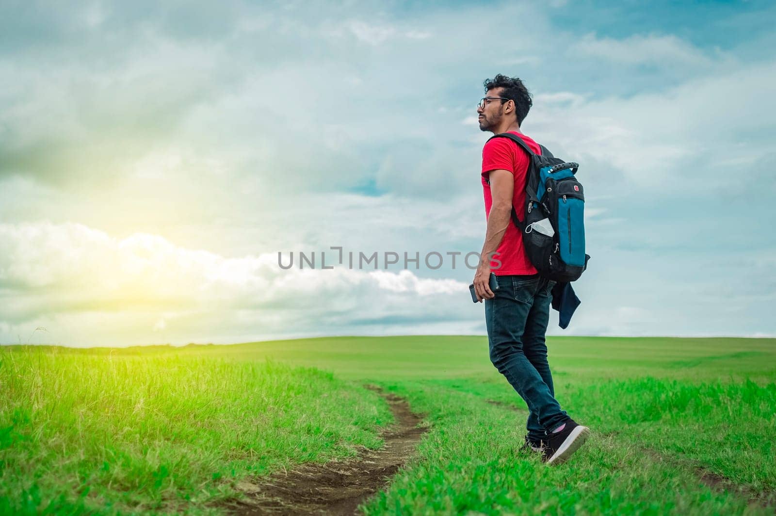 Side view of backpacking man on a beautiful road in the countryside. Young explorer man walking in a green field, Backpacker man walking in a beautiful field.