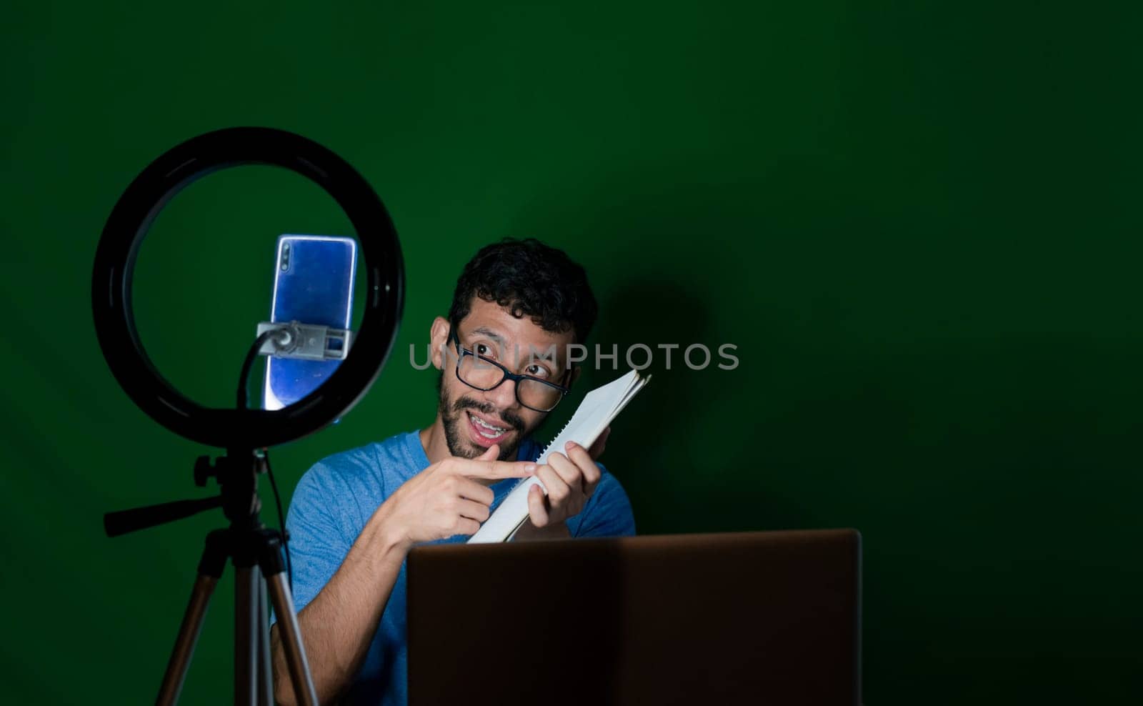 Person giving classes in a video call. Man giving online classes with phone. Guy with laptop making video blog on phone. Guy on a video call working from home. Online classes concept