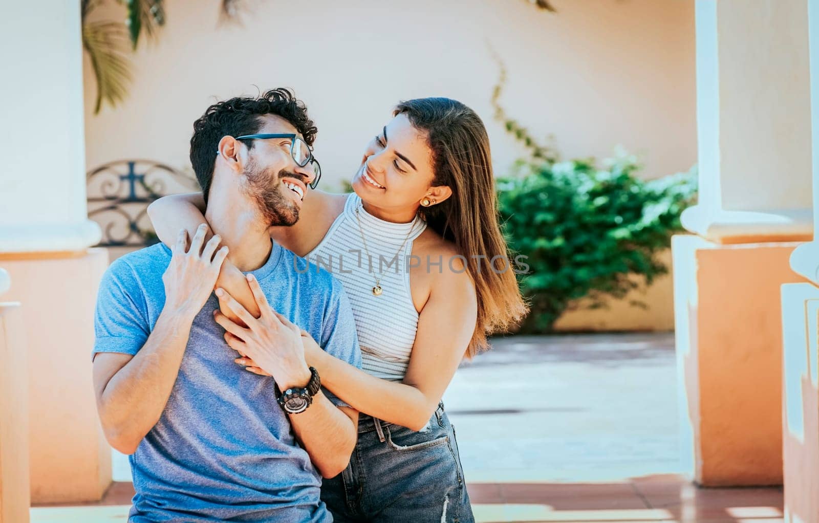 Girl hugging her boyfriend from behind. Smiling woman hugging her boyfriend from behind while he smiles at her, Happy couple, woman hugging man from behind outdoors