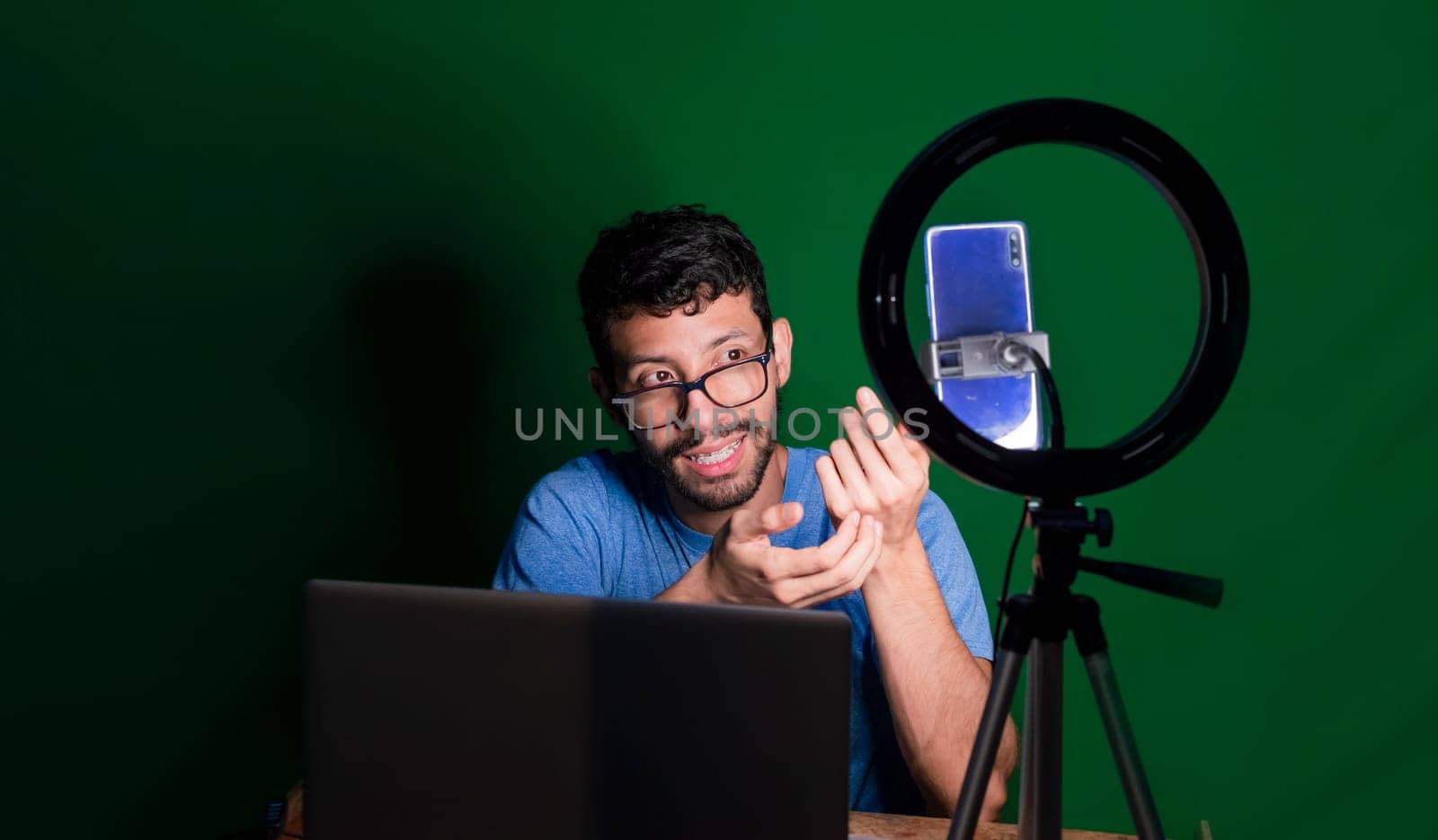 People giving online classes with phone. Guy with laptop making video blog on phone. Person giving classes in a video call. Guy on a video call working from home. Online classes concept