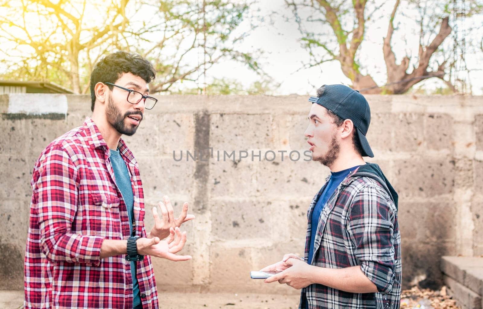 Two young friends talking face to face positively on the street. Side view of two young friends chatting outdoors, two friends having a positive talk while explaining things to each other