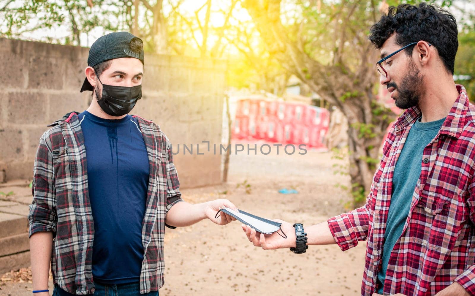Side view of young man giving a surgical mask to another person, concept of a person giving a surgical mask, Two young people giving each other a surgical mask