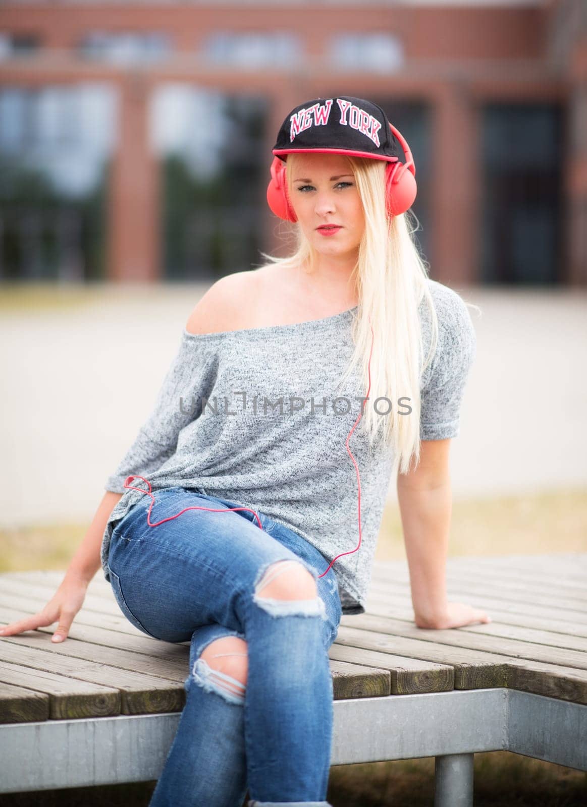Young woman in jeans sits outside listening to music