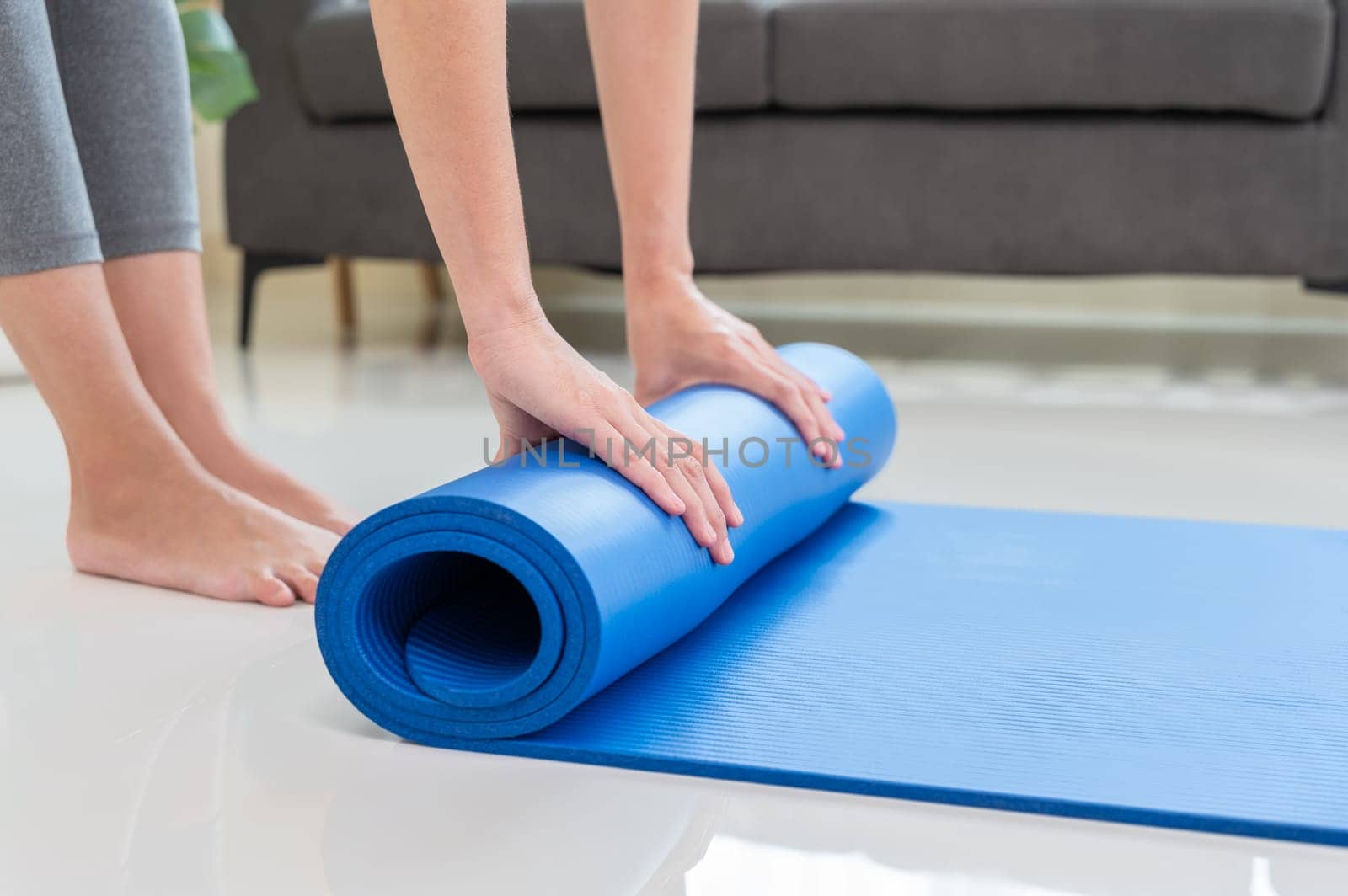 Cropped image of woman rolling blue mat after doing yoga exercise workout in living room at home. Healthy life and fitness training workout concept