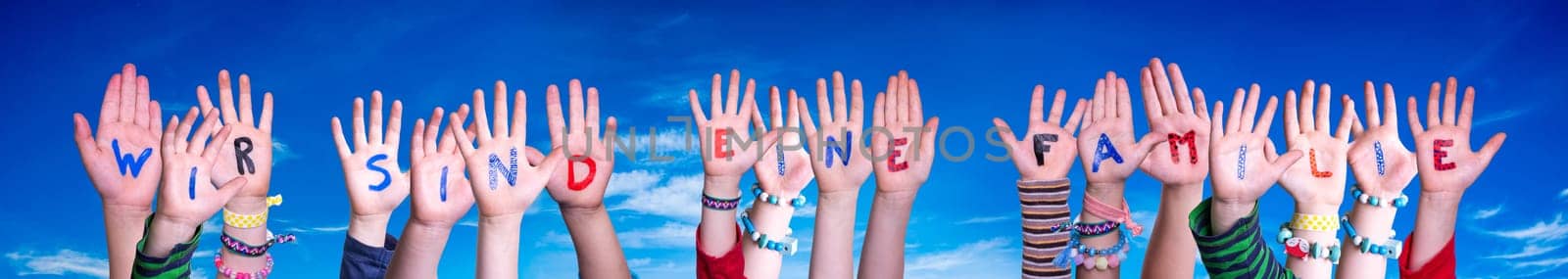 Children Hands Building Colorful German Word Wir Sind Eine Familie Means We Are Family. Blue Sky As Background.