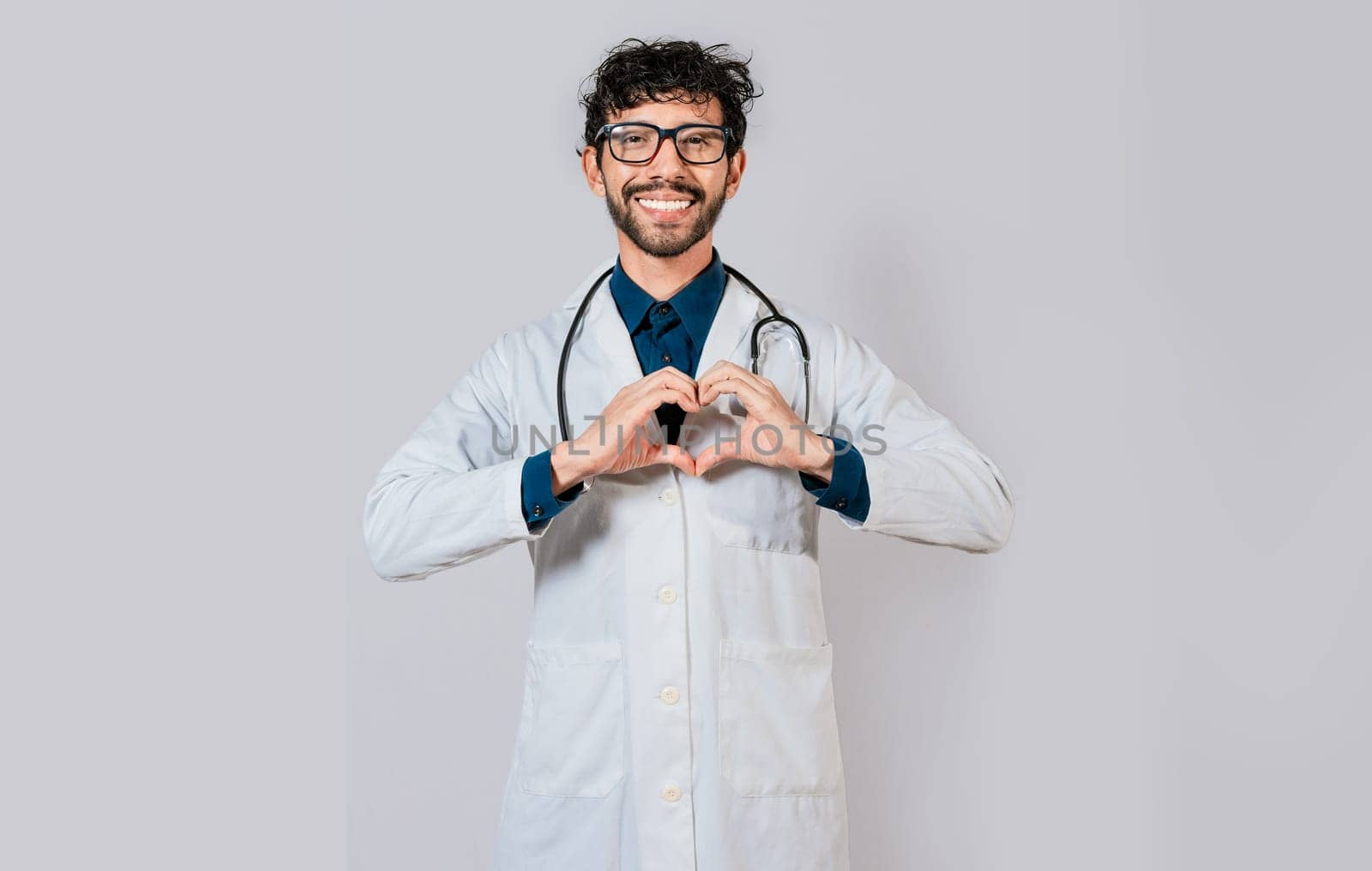 Young doctor making heart shape isolated. Handsome doctor making heart gesture with hands. Happy doctor pointing fingers down