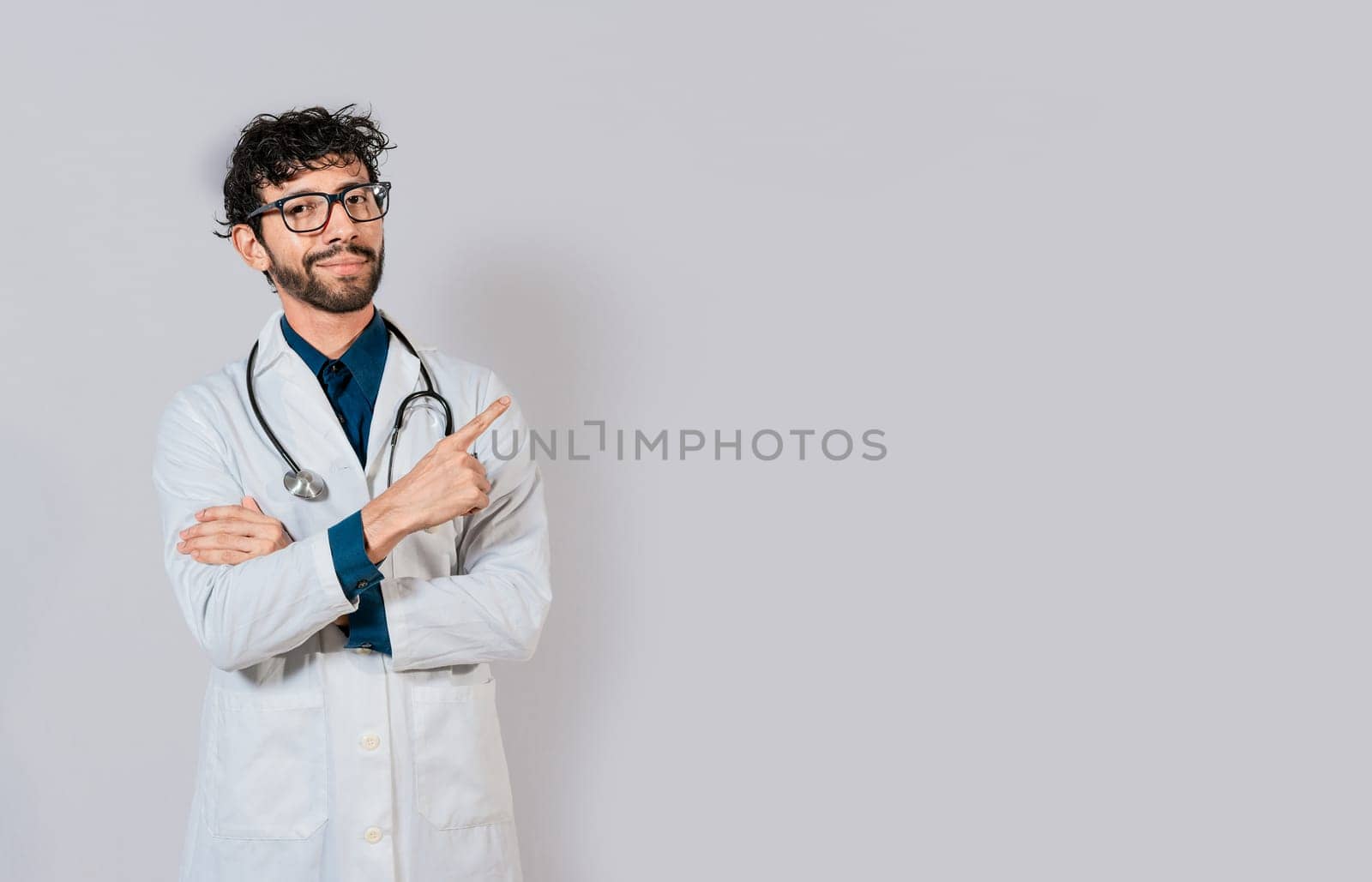 Smiling doctor pointing finger isolated. Doctor pointing at an isolated white space. Young doctor pointing finger at a blank space