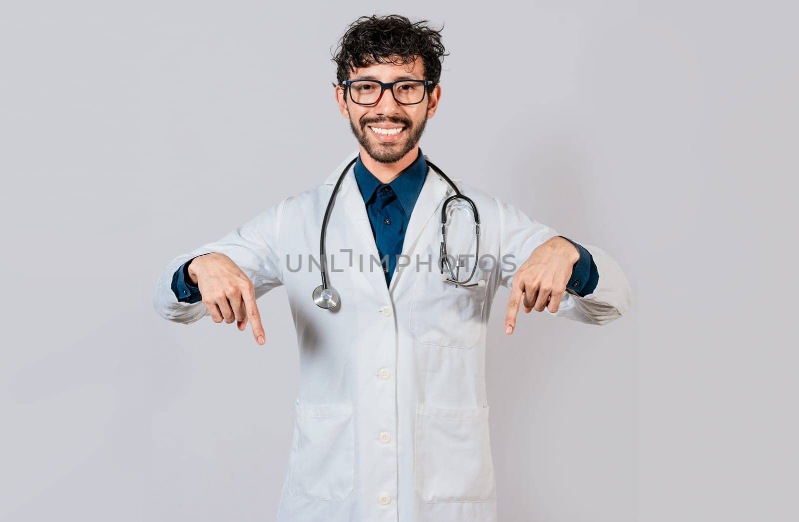 Young doctor pointing a promotion down. Handsome doctor pointing down an isolated advertising space. Happy doctor pointing fingers down
