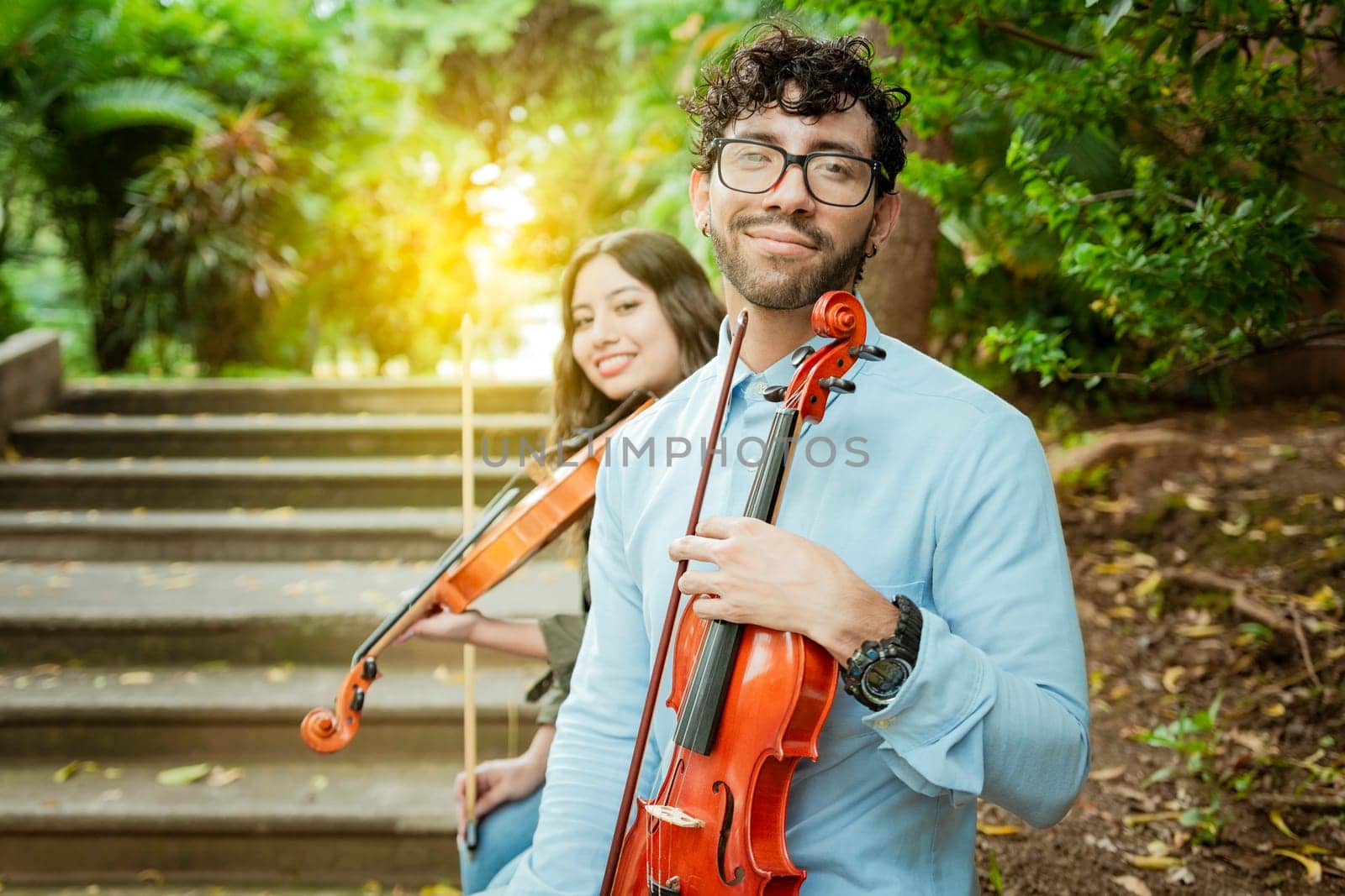 Portrait of two young violists sitting outside. Man and woman violinist sitting on the stairs. Concept of two young violinists, Two young violinists sitting outdoors looking at the camera