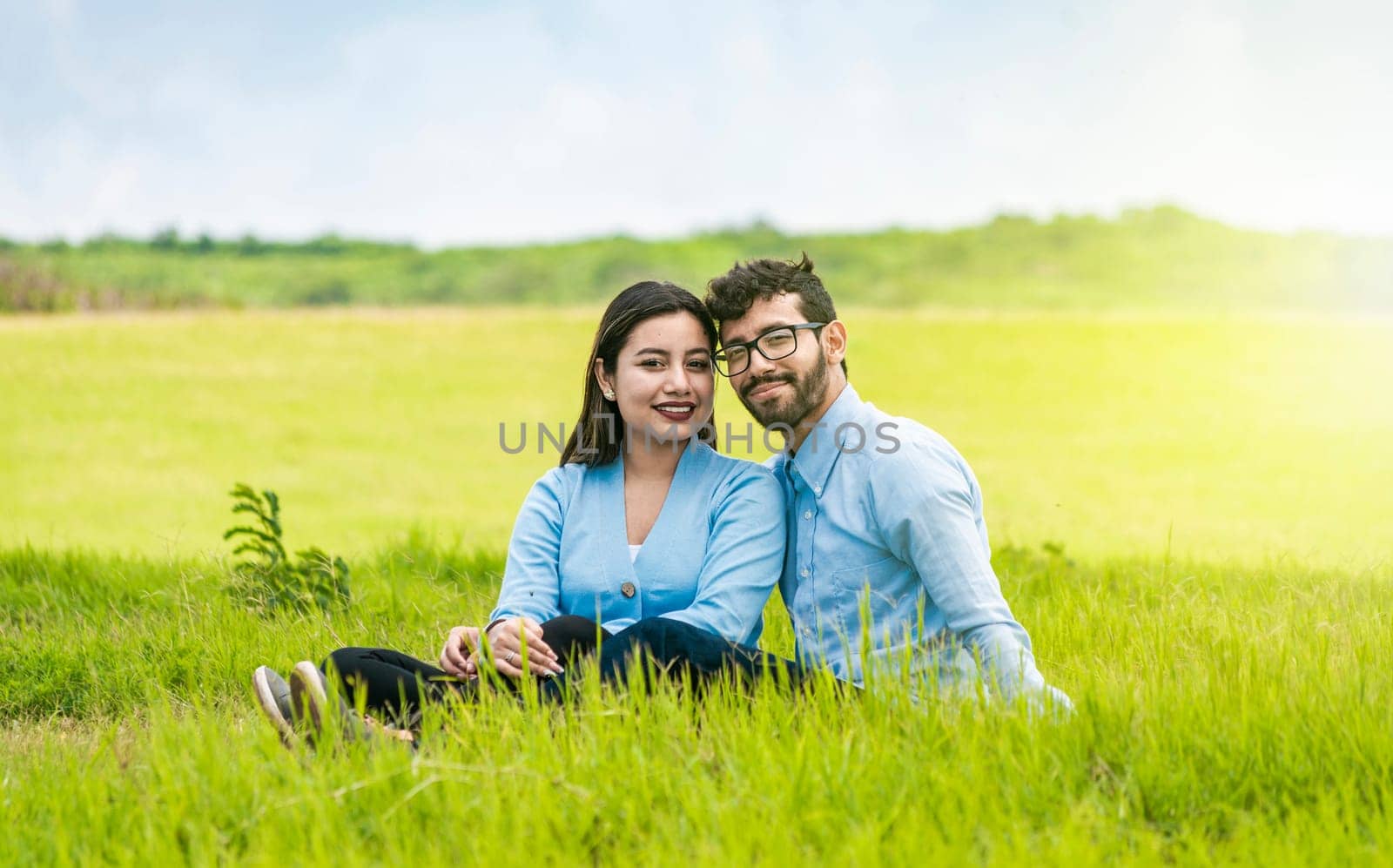 Young couple in love sitting on the grass looking at the camera, Two lovers sitting on the grass looking at the camera, Portrait of a couple in love sitting on the grass in the field