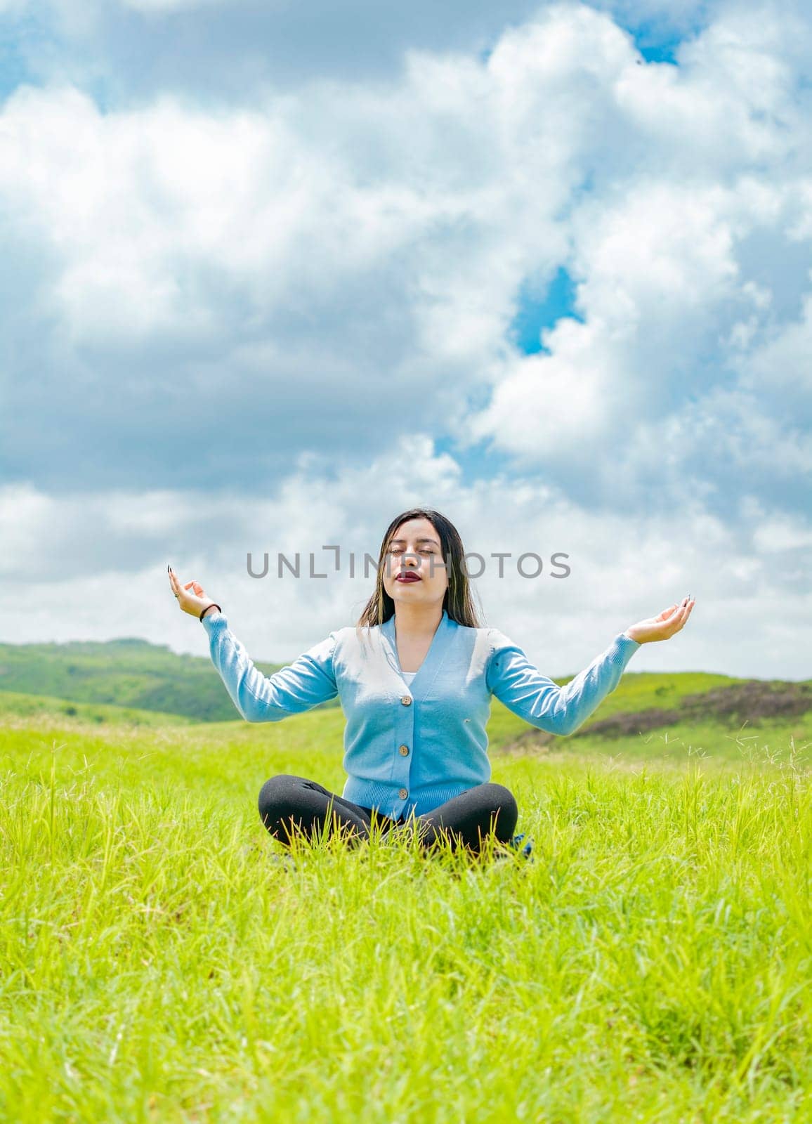 Young woman doing yoga on the grass in the field with blue sky in the background, Girl sitting doing meditation yoga in the field, woman doing yoga outdoors