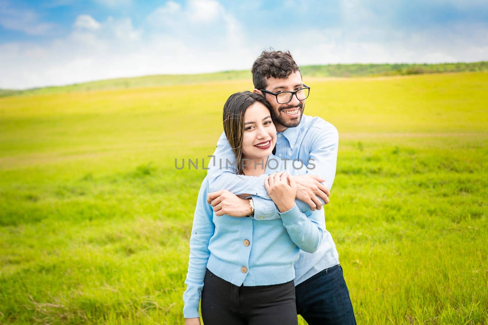 Portrait of a happy couple hugging in the field, Portrait of a young couple in love in the green field looking at the camera, Portrait of a cute couple in the field looking at the camera