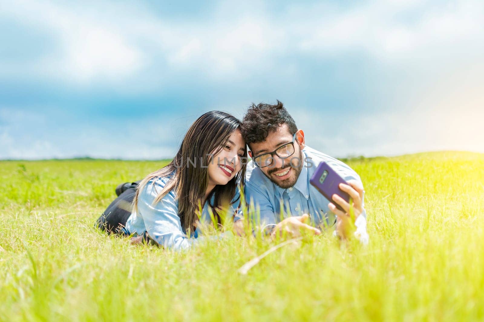 A couple lying on the grass taking a selfie, young couple in love lying on the grass taking a selfie, two people in love lying on the grass taking selfies