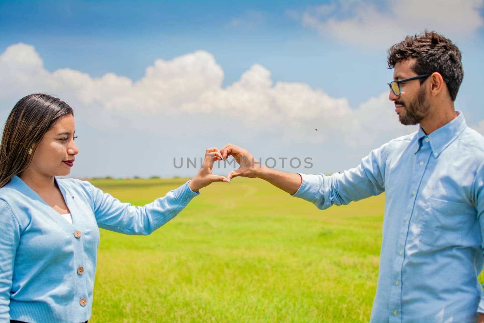 Happy couple making a heart shape with their hands, couple in love in the field making a heart shape with hands, beautiful couple in the field making a heart shape with hands