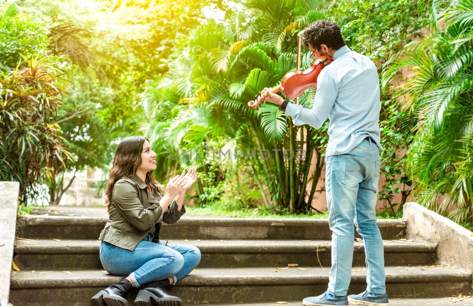 Violinist man playing a melody to a girl sitting on the stairs. Man playing violin for girl sitting on stairs outside. Concept of man playing violin to people on the street