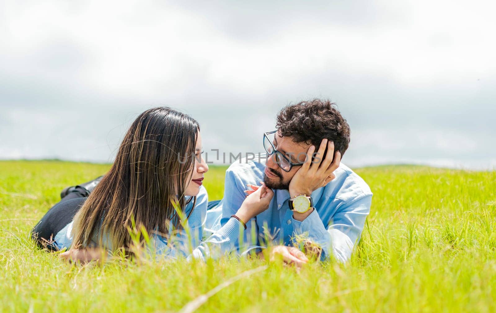 Two people in love lying on the grass looking at each other, A couple lying on the grass looking at each other, Young couple in love lying on the grass touching each other's faces