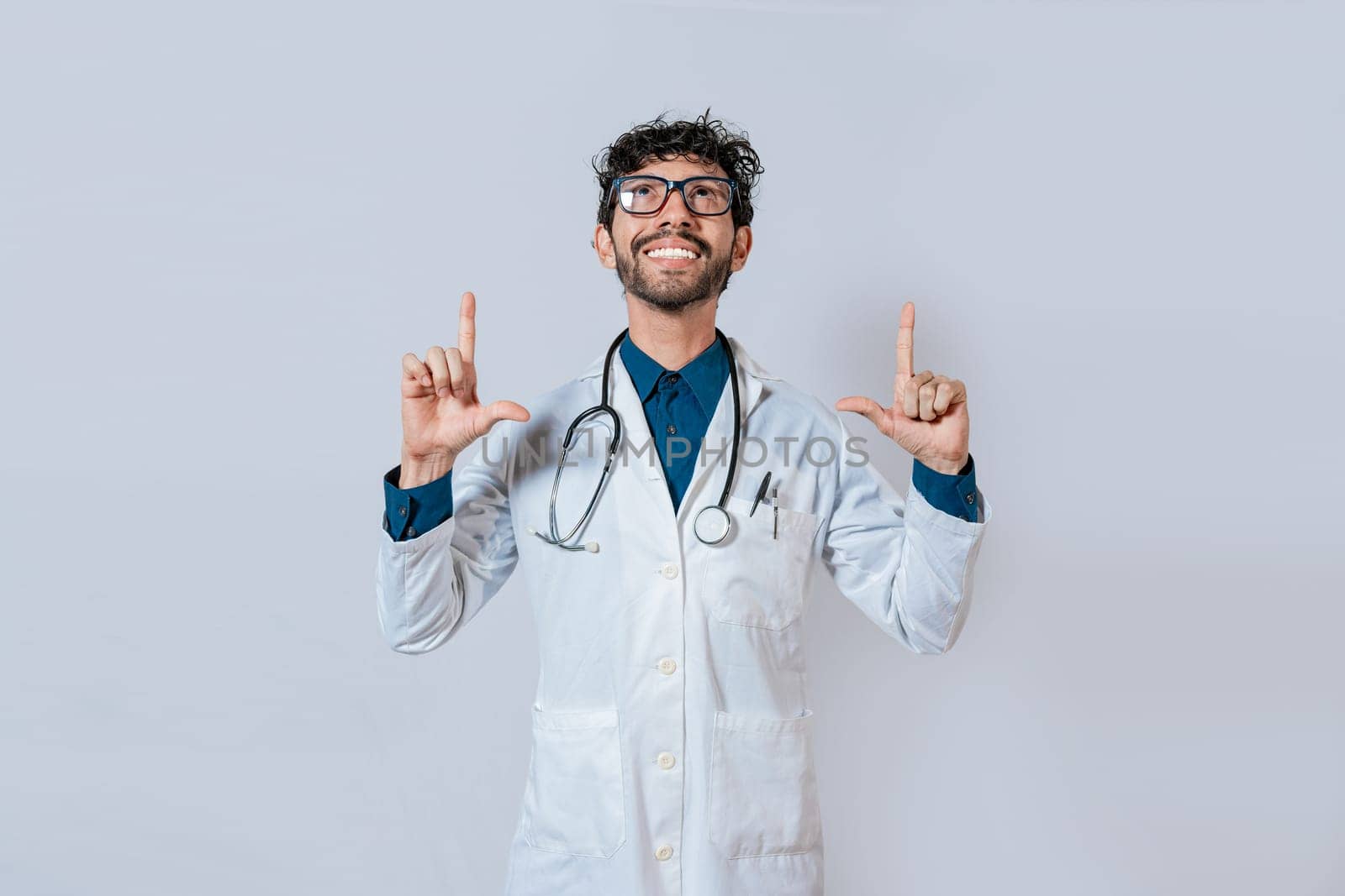 Handsome doctor pointing up. Smiling doctor pointing a promo up. Male doctor looking and pointing up isolated