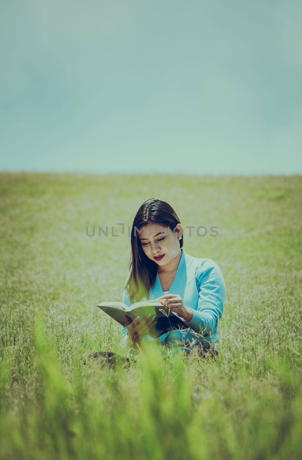 A person sitting on the grass reading a book, Attractive people sitting on the grass reading a book, A girl reading a book in the field
