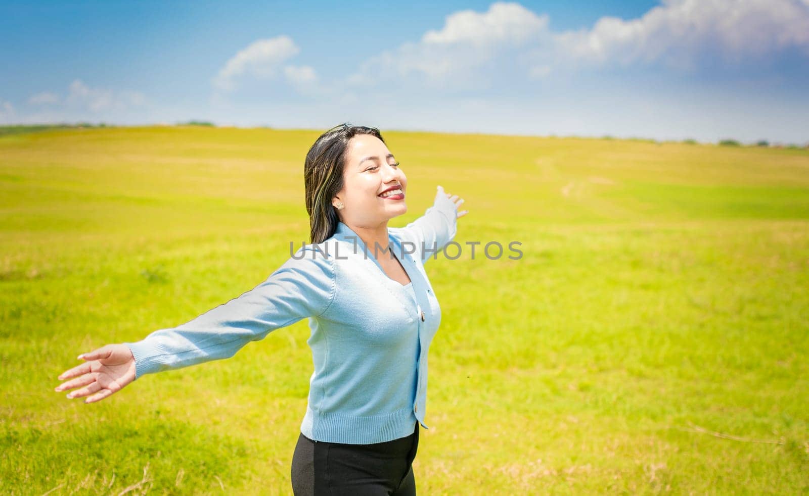 Young woman smiling and spreading her hands in the green field, concept of woman breathing fresh air in the field, Happy woman breathing fresh air in the field and spreading arms