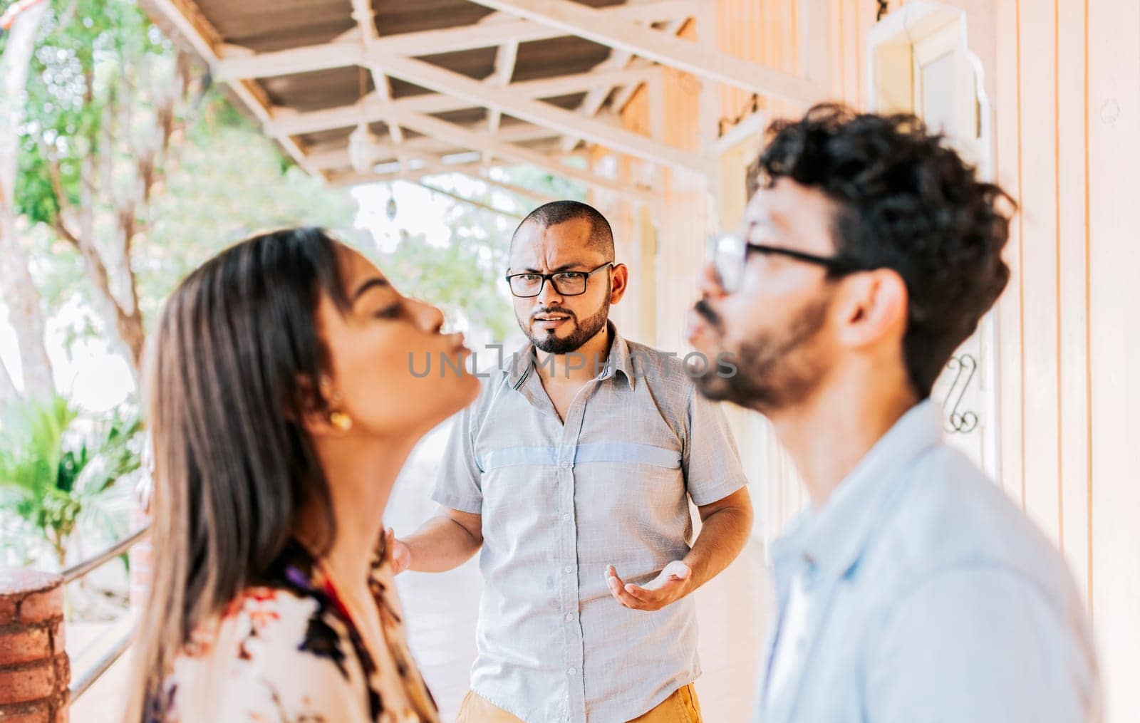 Man discovering his cheating girlfriend kissing another man in the street, Boyfriend discovering his girlfriend's infidelity outdoors. Man looking at his cheating girlfriend kissing another woman outdoors