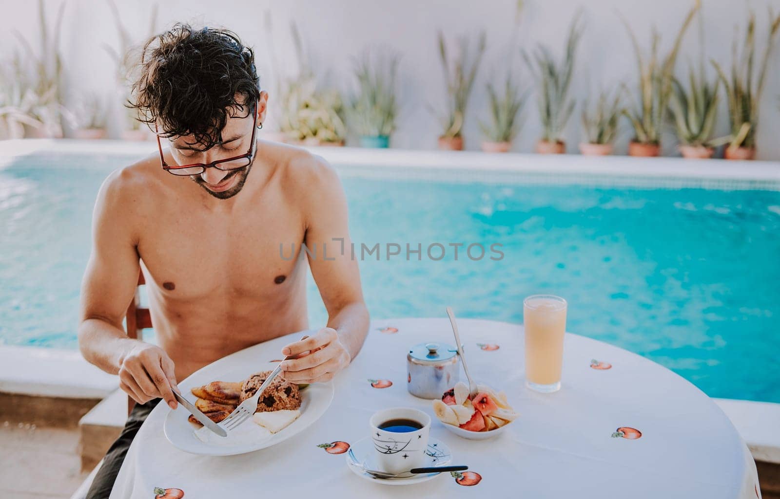 Young man on vacation in hotel having breakfast near swimming pool. Breakfast near the swimming pool. Person having breakfast in the hotel with pool in the background