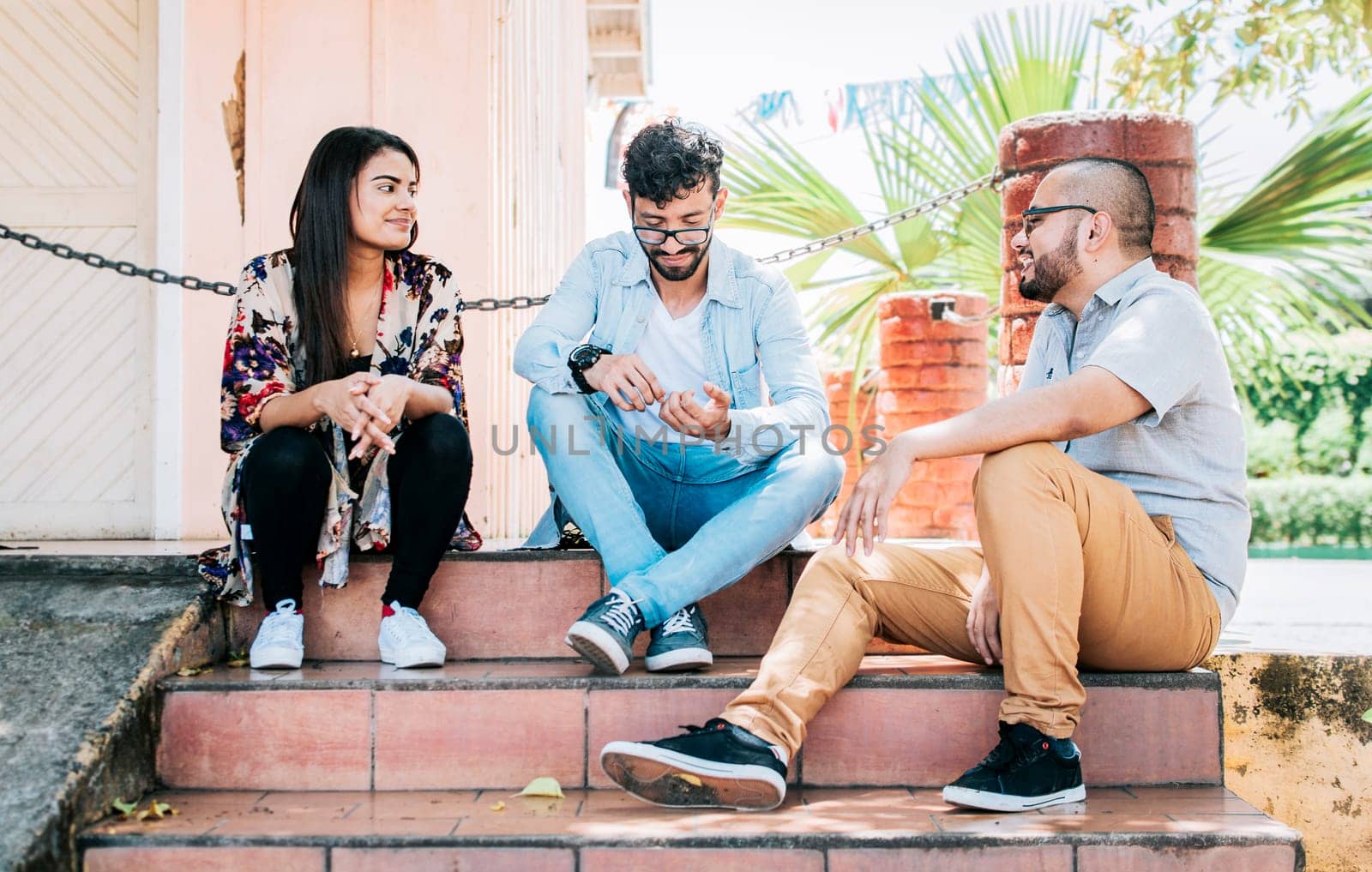 Three teenage friends talking sitting on the stairs, Three young people sitting on the street talking. Concept of friends talking, Three young friends talking sitting on the stairs