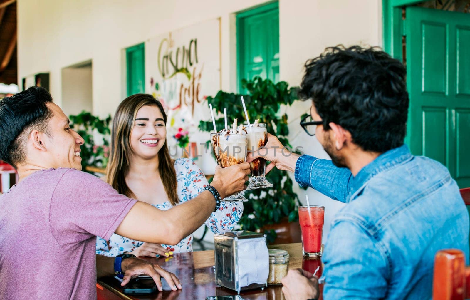 Happy friends enjoying a milkshake in a coffee shop. Three happy best friends meeting and toasting in a coffee shop, Happy young friends toasting in a coffee shop