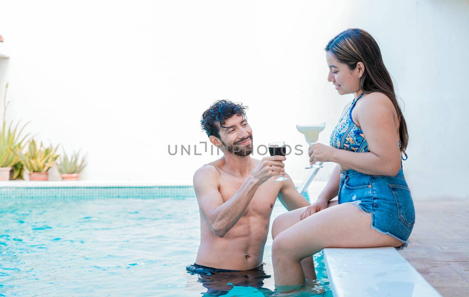Smiling couple enjoying and toasting in swimming pool. Young man and woman on vacation toasting in the pool, Young couple on vacation toasting and talking in swimming pool