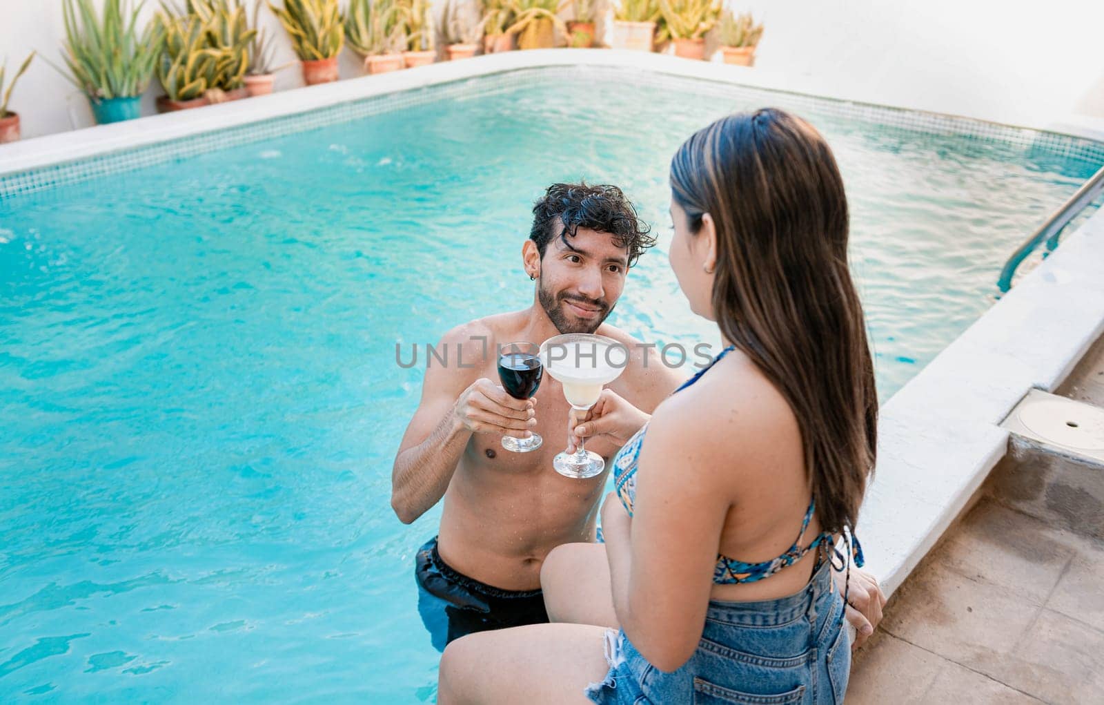 Young couple on vacation toasting and talking in swimming pool, Smiling couple toasting in swimming pool. Young man and woman on vacation toasting in the pool