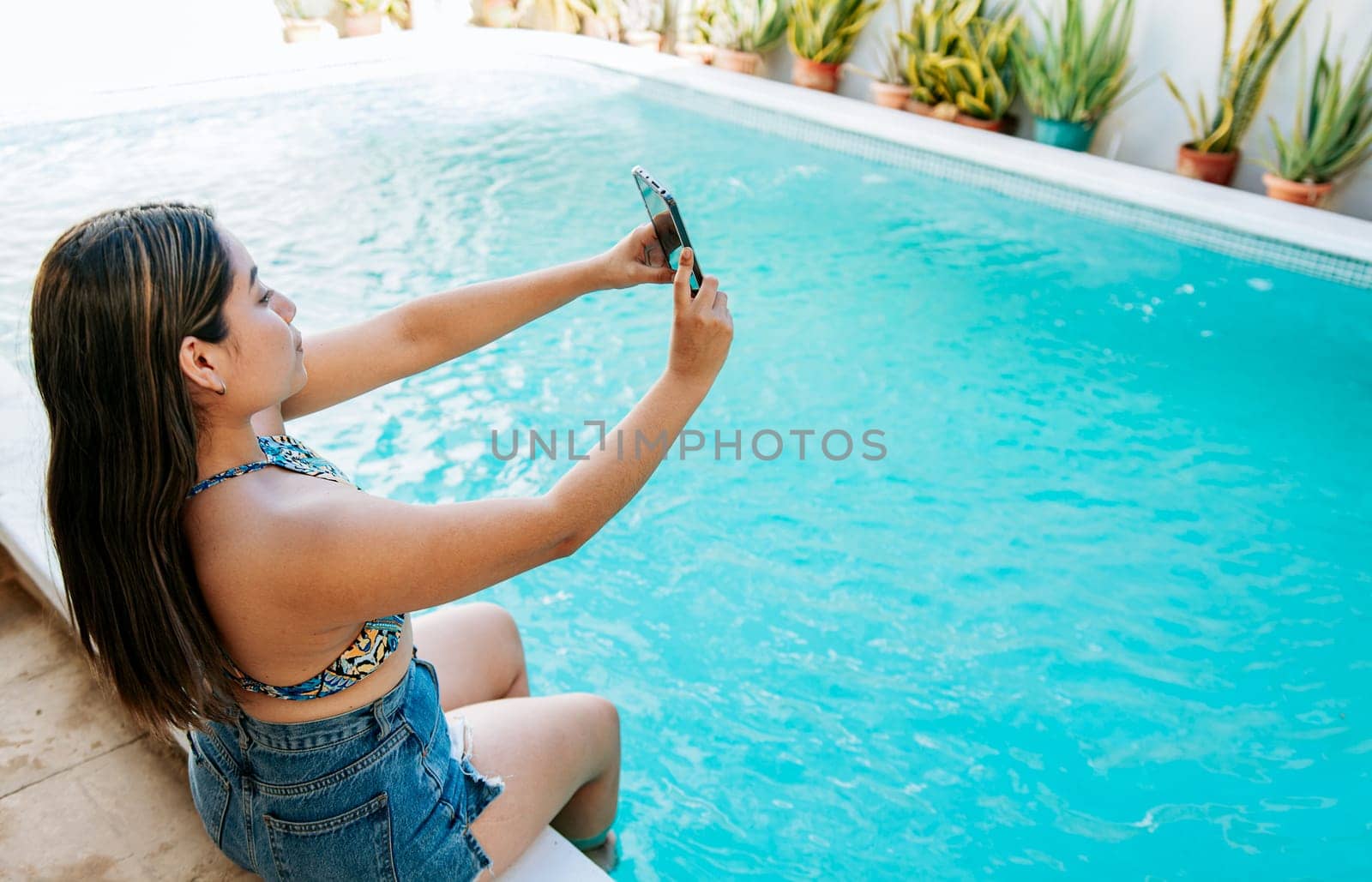 Girl on vacation at the edge of the swimming pool taking a selfie. Attractive girl on vacation in the swimming pool taking a selfie