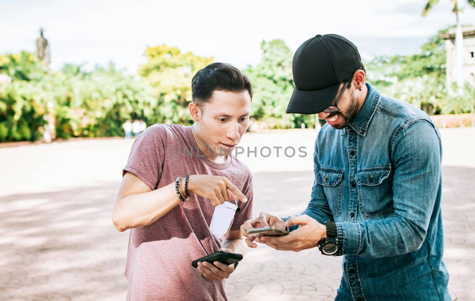 Two teenage guys checking their cell phones in the street, Two guys checking a cell phone outdoors, Two young men looking media on a cell phone in the street