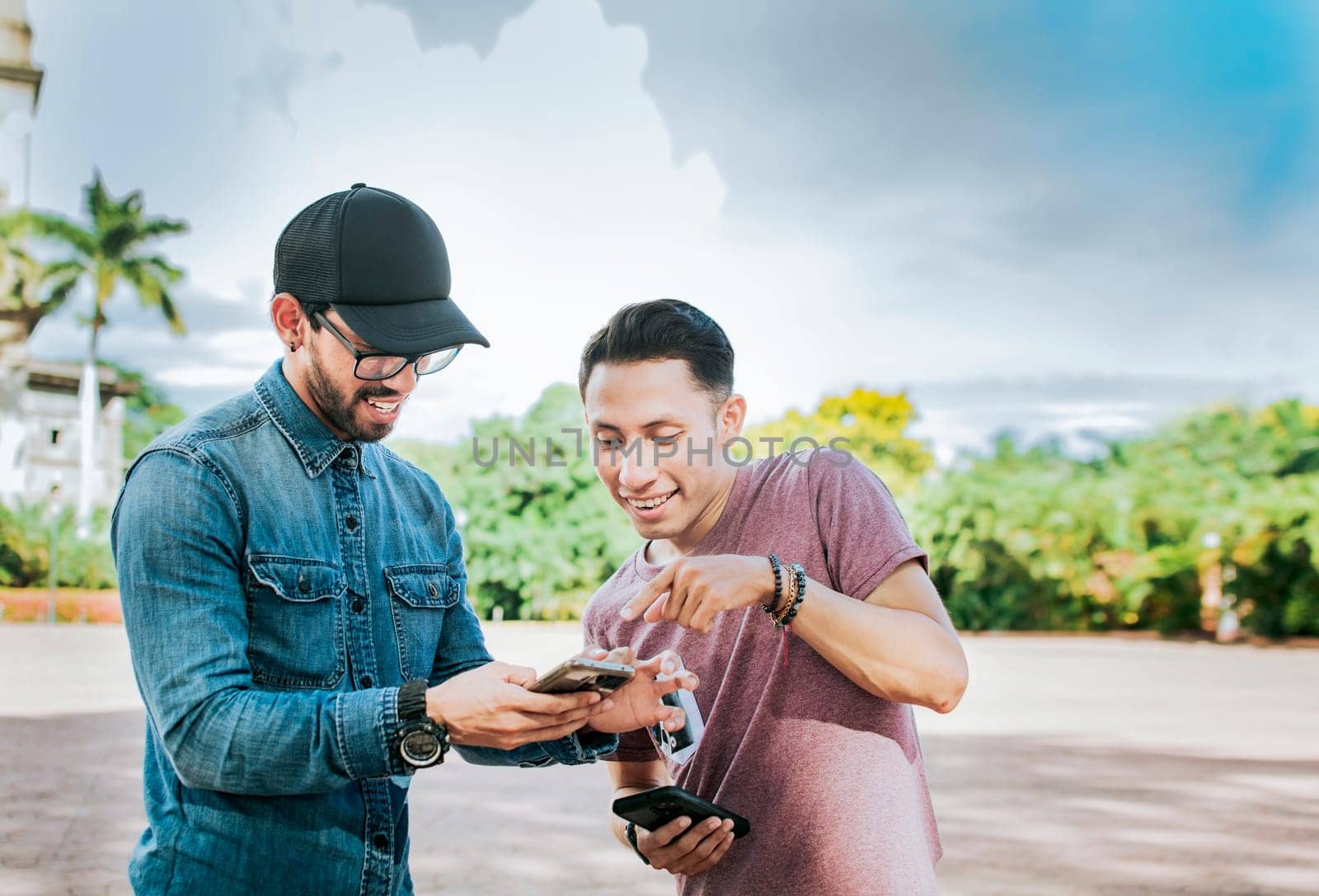 Two young friends having fun with the cell phone outdoors. Two happy friends looking at a cell phone in the street, Two smiling friends looking at media on the cell phone in the street