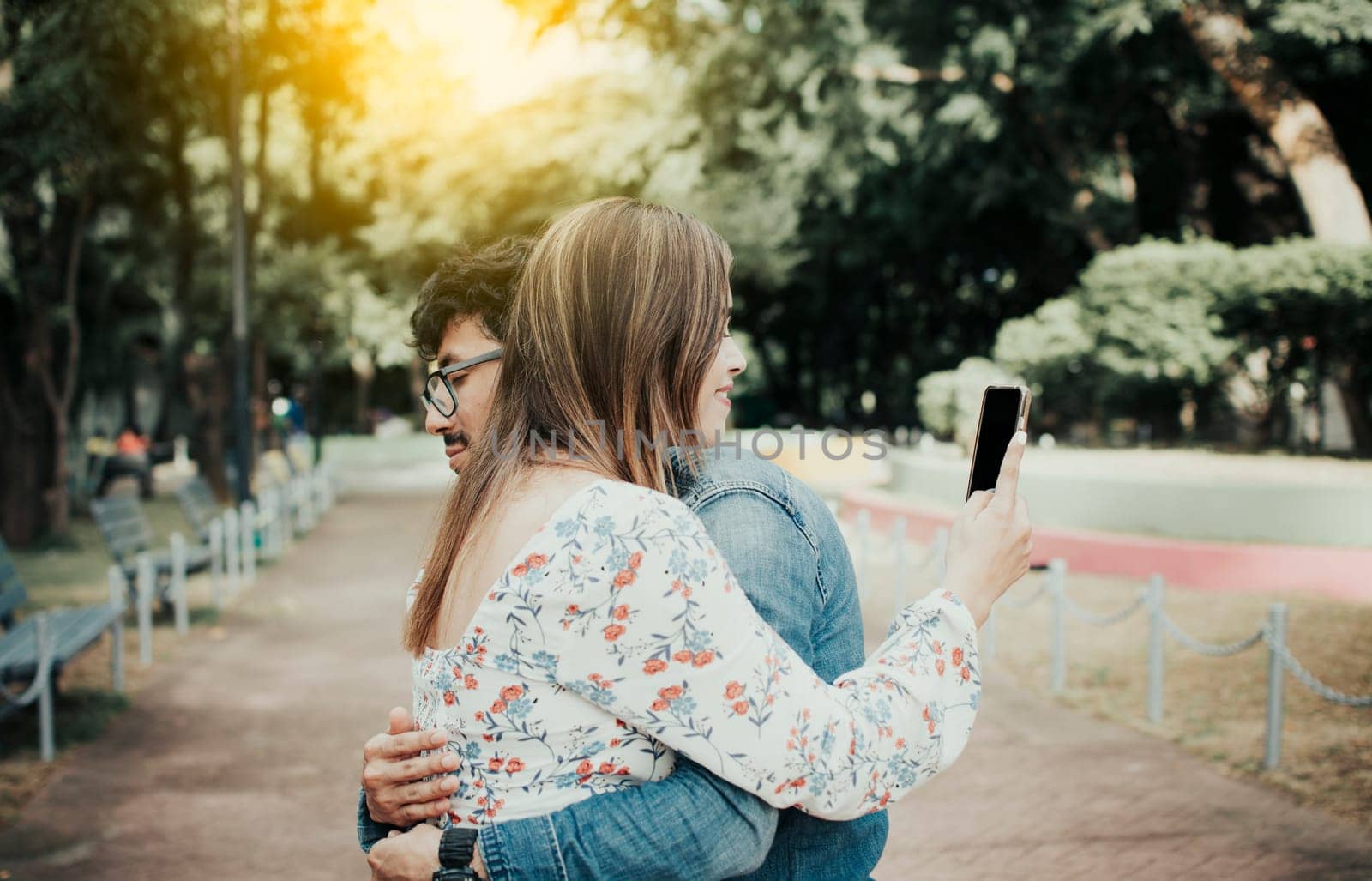 Cheating girlfriend hugging boyfriend and looking at cell phone. Unfaithful woman looking at cell phone while hugging boyfriend. Girl addicted to cell phone hugging boyfriend