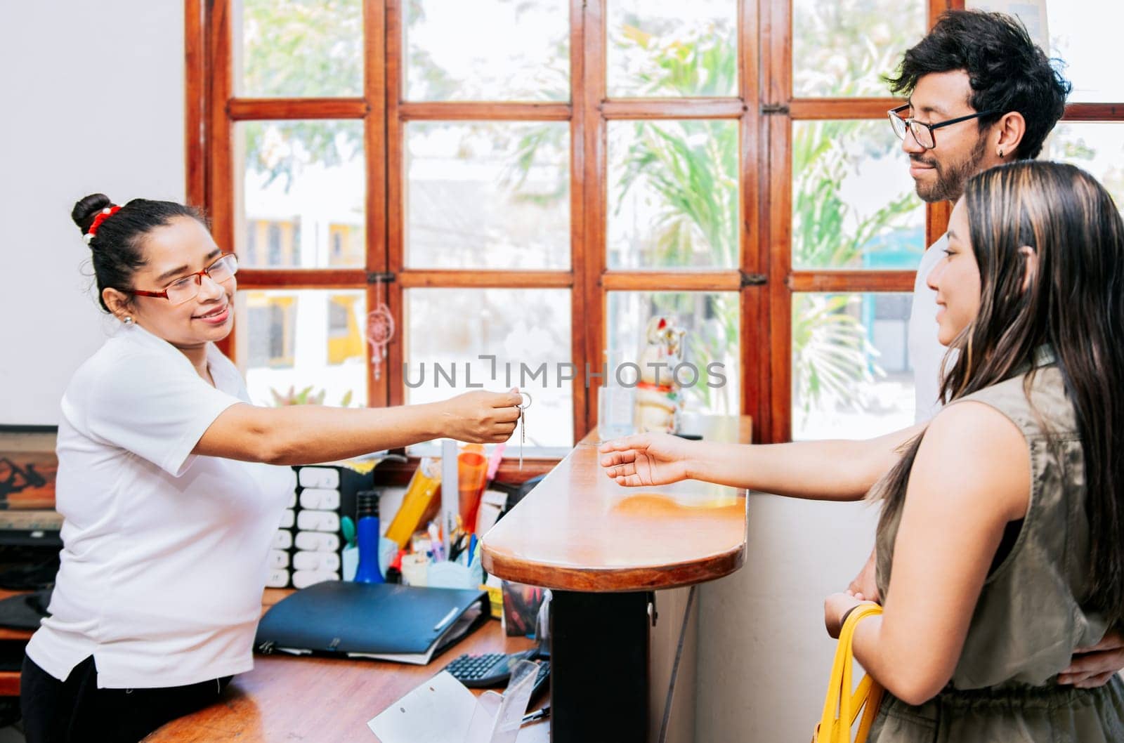 Latin couple receiving hotel room keys. Woman receptionist giving hotel room key to couple, Concept of couple arriving at hotel, Receptionist giving hotel room keys to couple