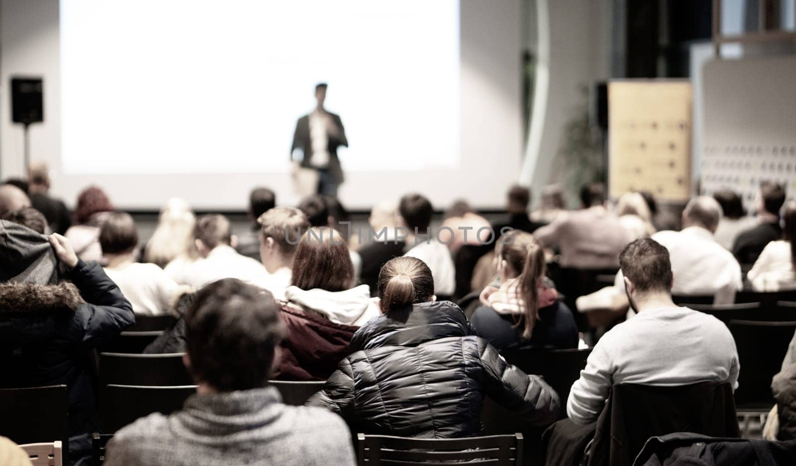 Speaker giving a talk in conference hall at business event. Rear view of unrecognizable people in audience at the conference hall. Business and entrepreneurship concept.