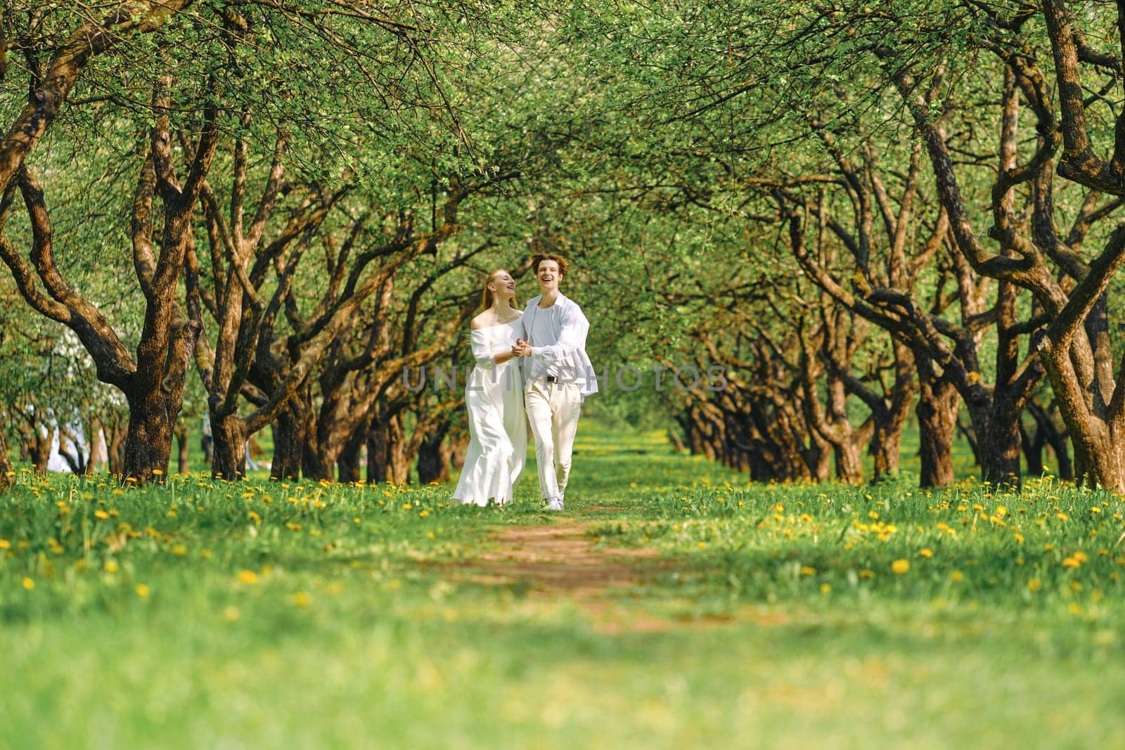 Happy newlyweds in white clothes hold hands of each other and dancing in the park