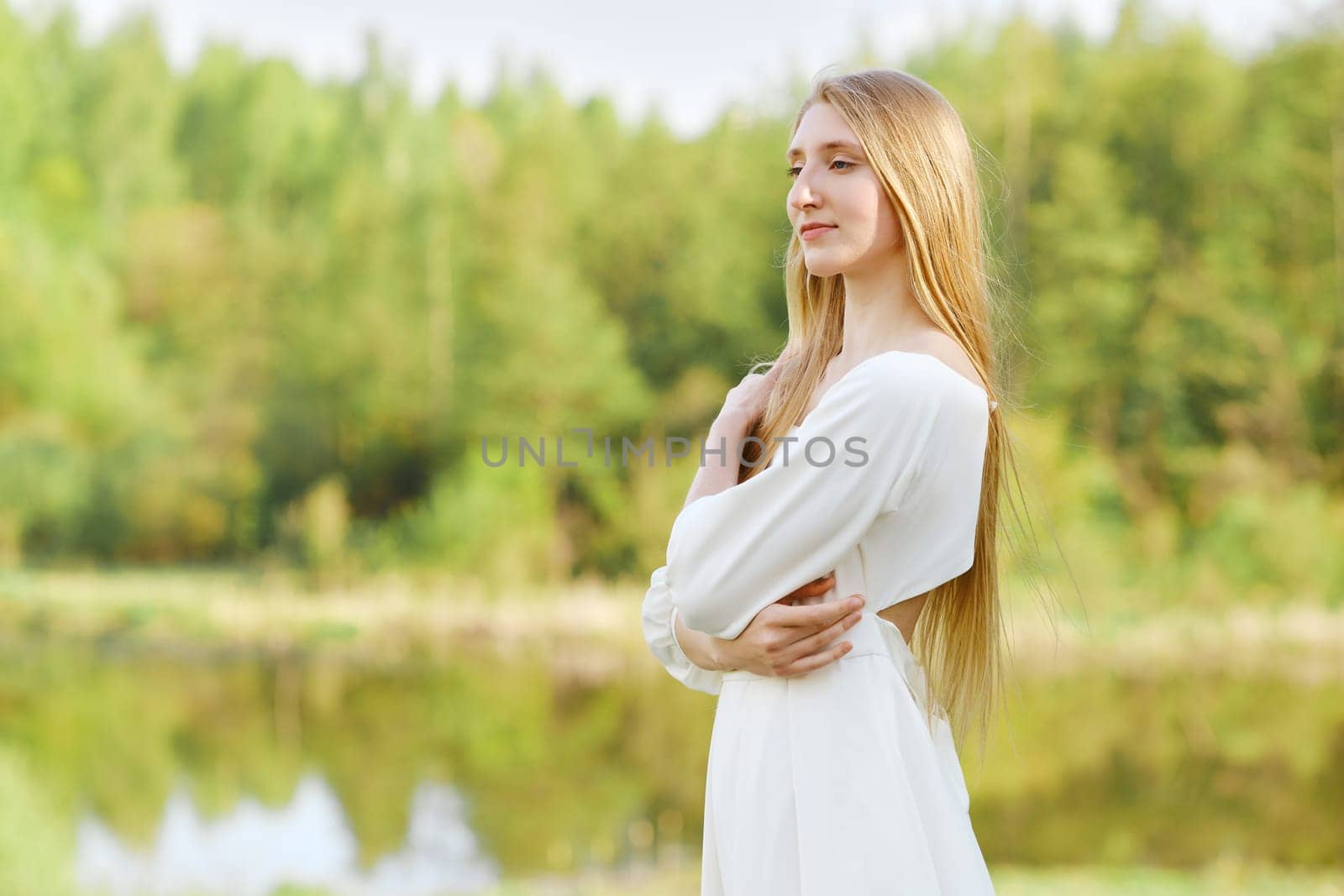 Beautiful woman in white dress on river bank with crossed arms