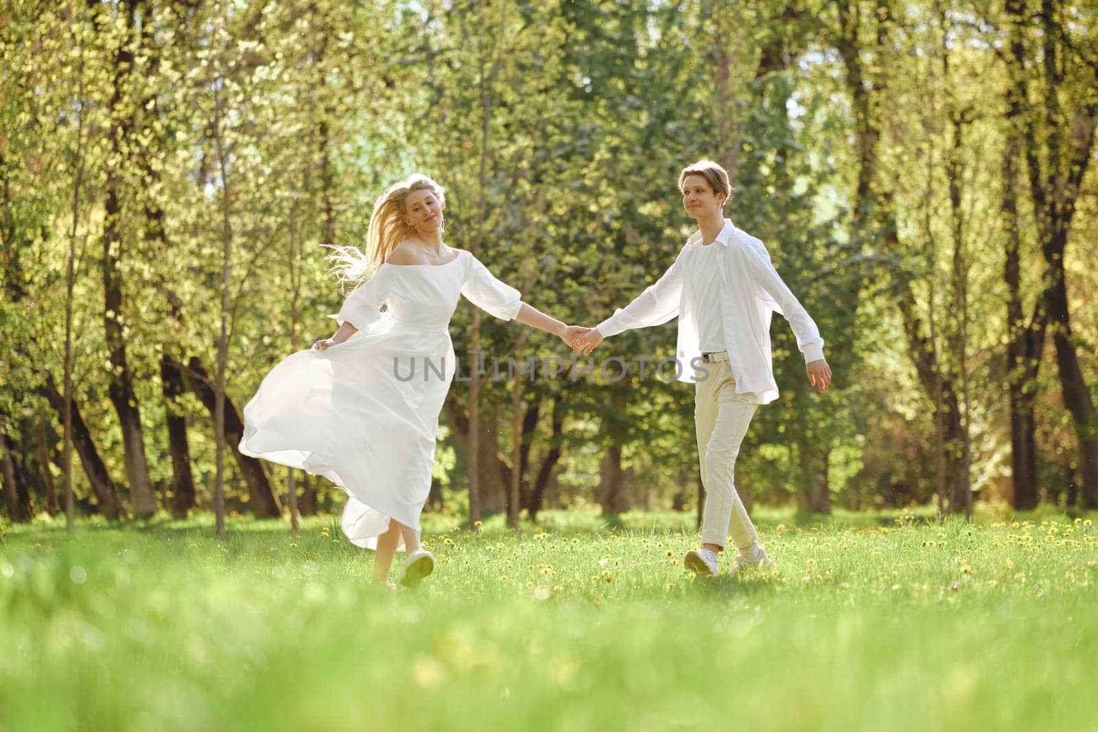 Happy newlyweds holding hands and dancing on the lawn in sunny day