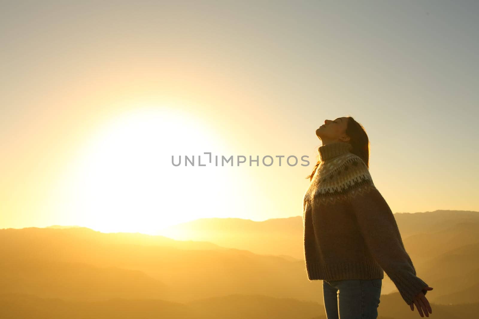 Side view portrait of a relaxed woman breathing fresh air at sunset in the mountain in winter