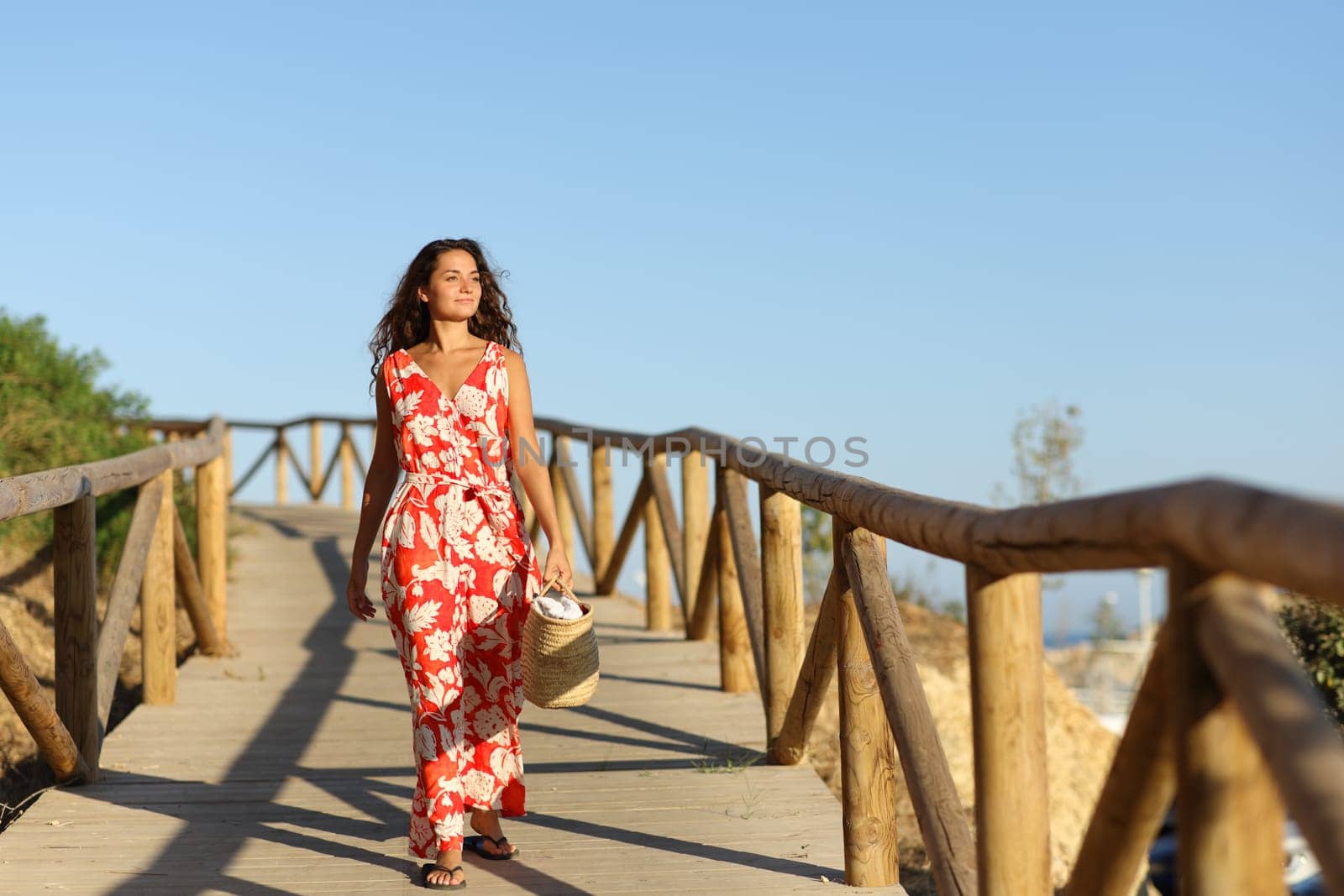 Front view full body portrait of a happy woman in red walking to the beach