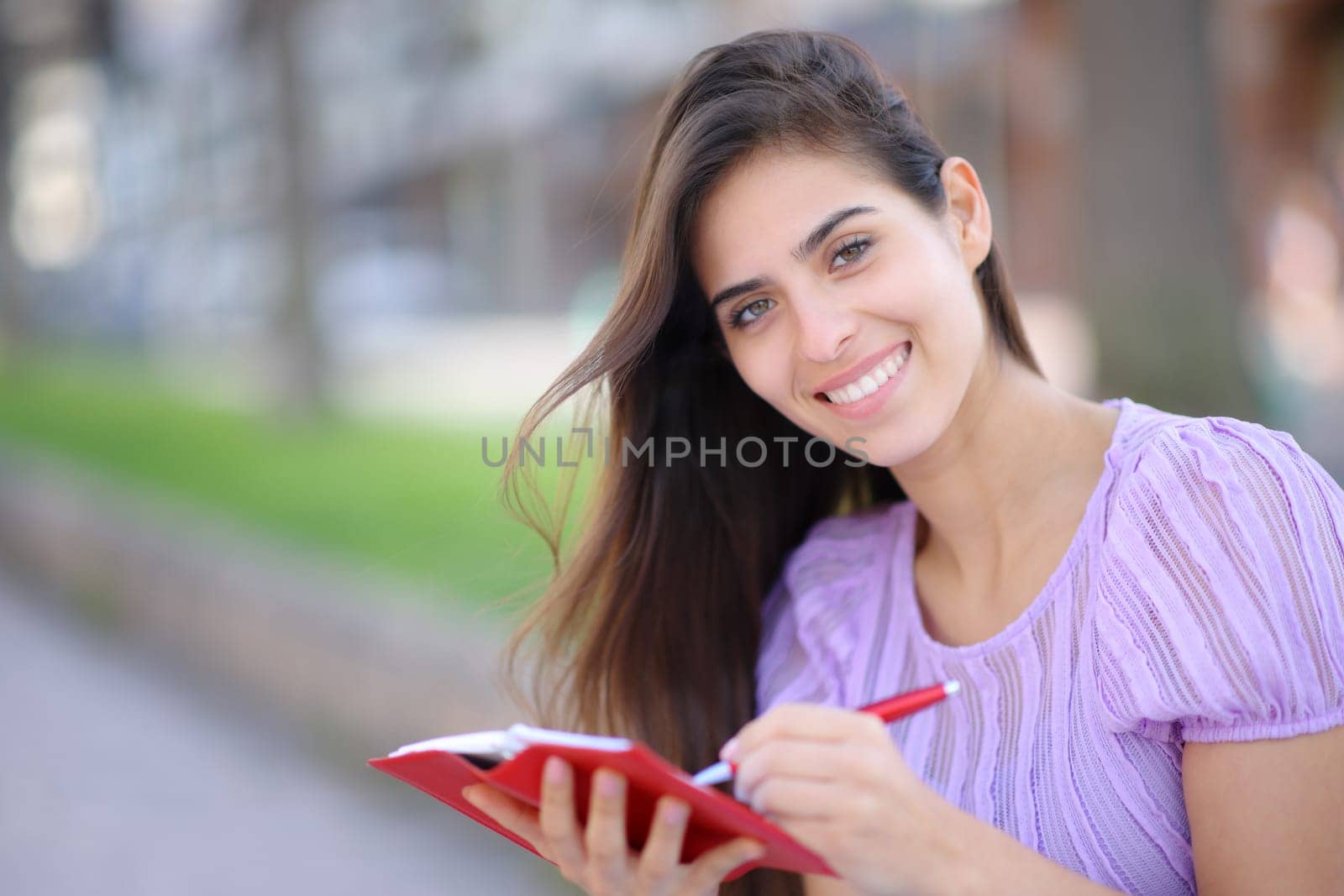 Happy woman writing in paper agenda looks at you in the street