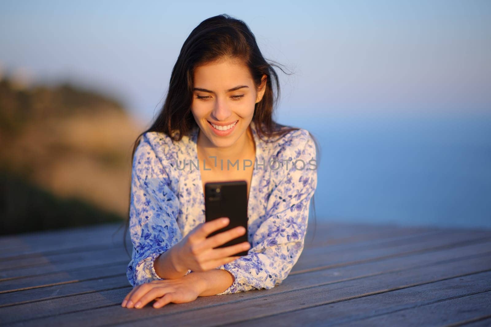 Front view portrait of a happy woman on the beach using cell phone