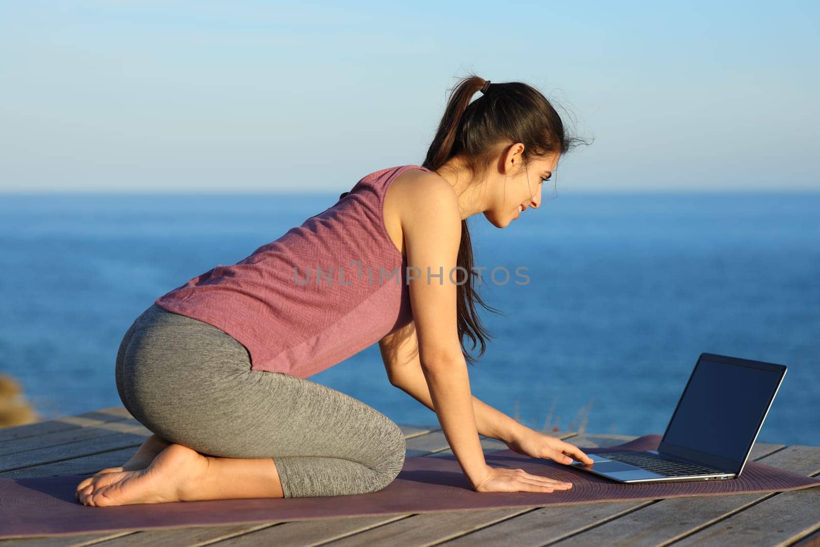 Sportswoman using laptop to learn yoga exercises on the beach