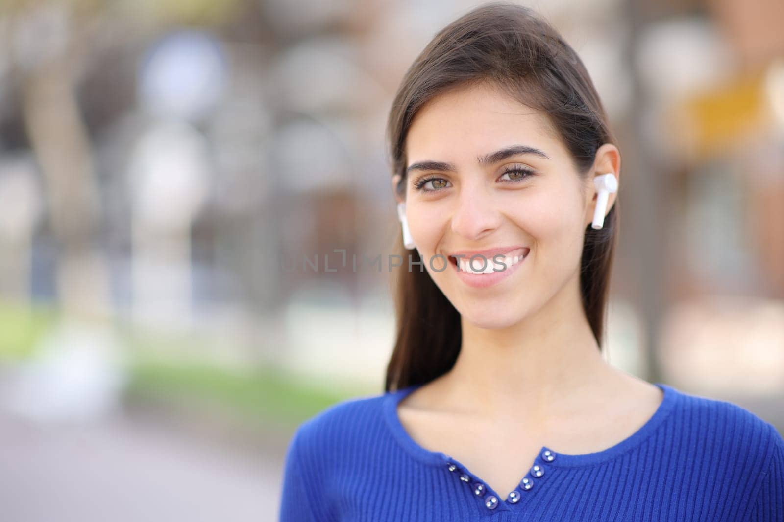 Happy woman with earphone standing and posing looking at camera in the street