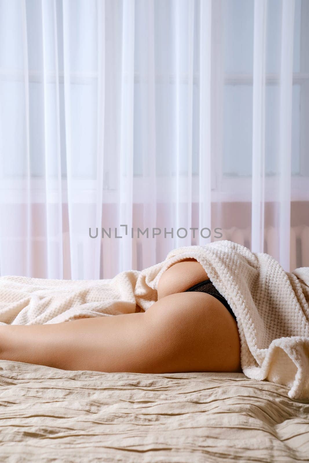 Concept of a comfortable sleep: a woman's leg, hip and buttocks on an orthopedic mattress sticking out of a blanket