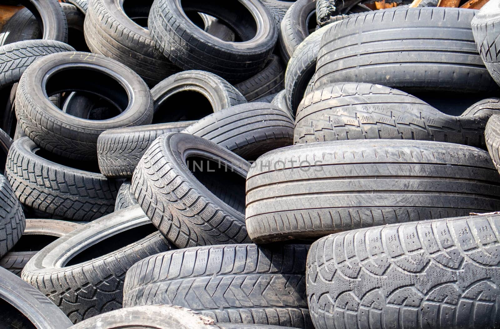 Garbage from a pile of black old car tires. Environmental pollution. Ecological problems. Old car tires thrown into an industrial landfill for recycling. Reuse of worn rubber tires
