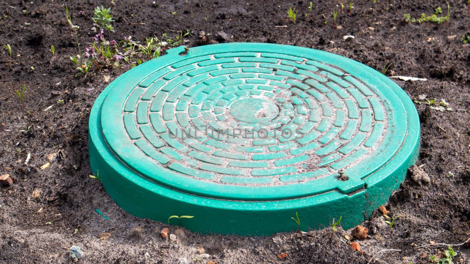 New green metal manhole on the land. Repair work. The closed sunroof does not pose a danger to pedestrians and vehicles. Underground pipeline repair